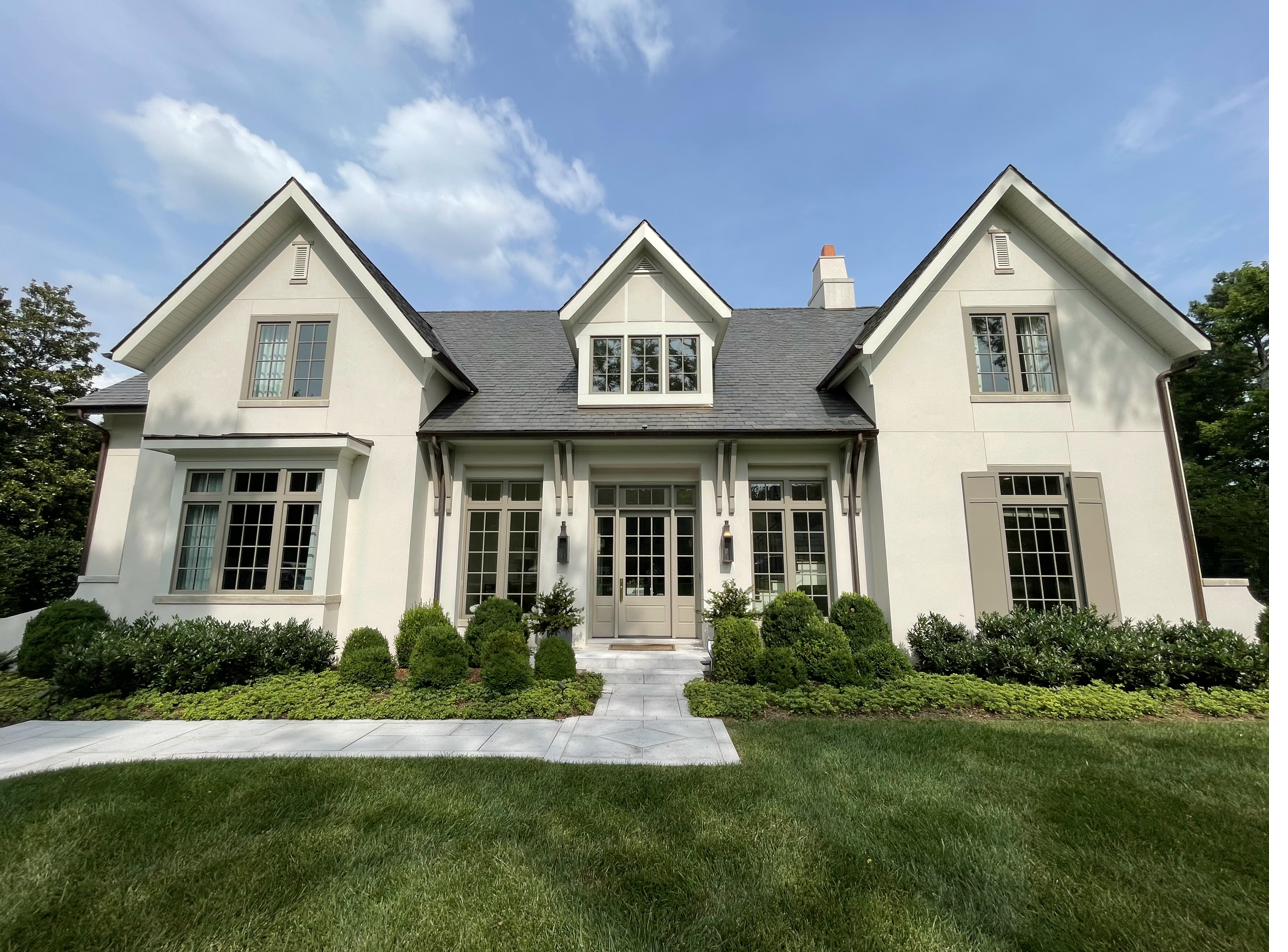 Cream stucco home with manicured boxwood layered foundation plantings and emerald lawn