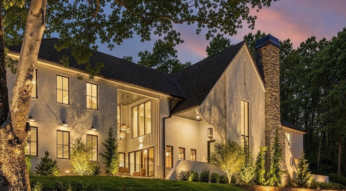 Forest Hills estate hillside at twilight with uplit sycamore, columnar evergreens, and boxwood plantings lit along a stone retaining wall