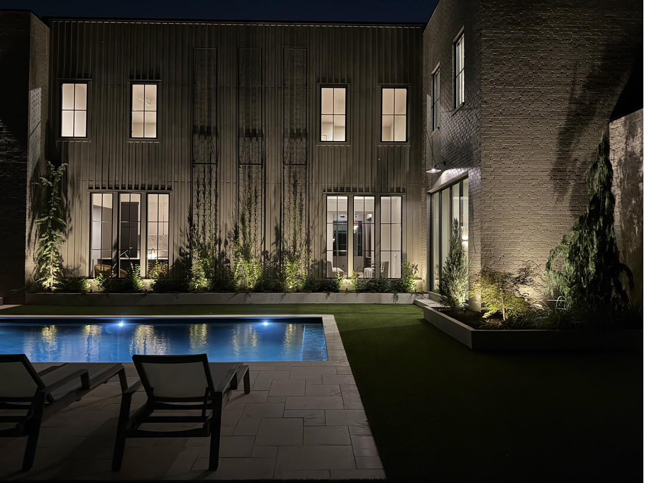 Modern courtyard with uplit columnar plantings and blue pool at night