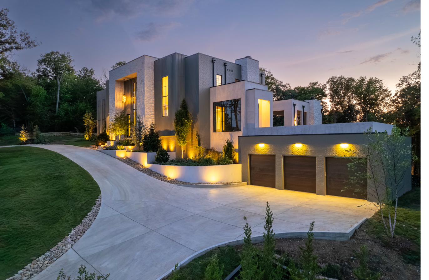Modern estate driveway approach with landscape lighting and tiered planting beds at dusk