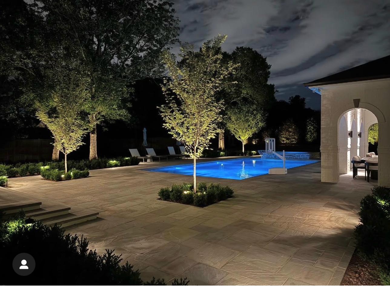 Pool area with uplighted trees and boxwood plantings at night in Nashville