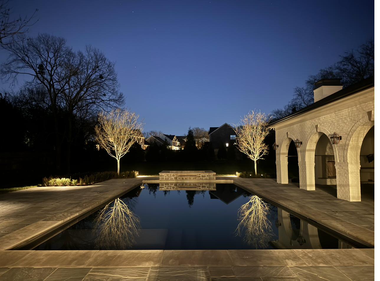 Reflecting pool with uplit winter trees and arched stone pool house