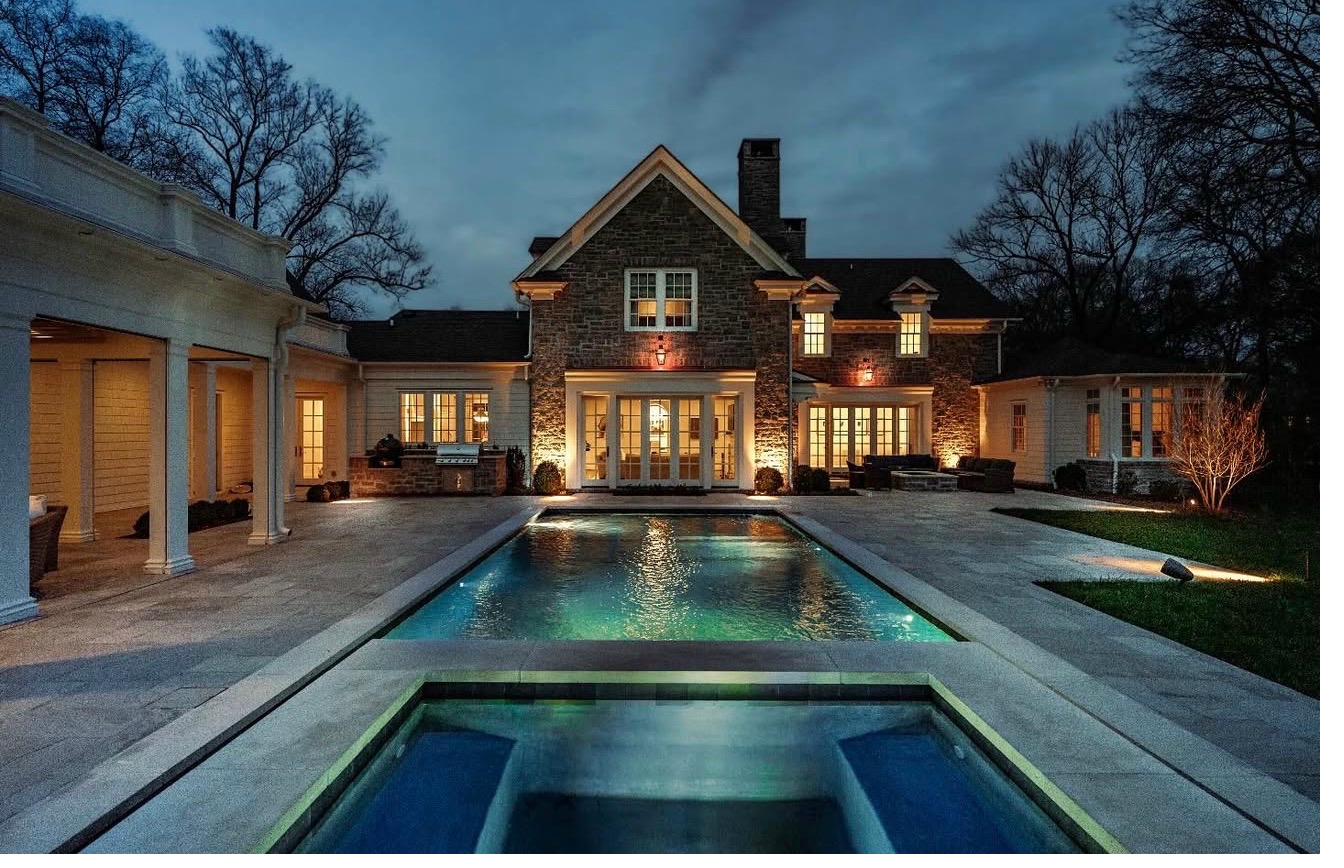 Reflecting pool with uplit winter trees and arched stone pool house at blue hour
