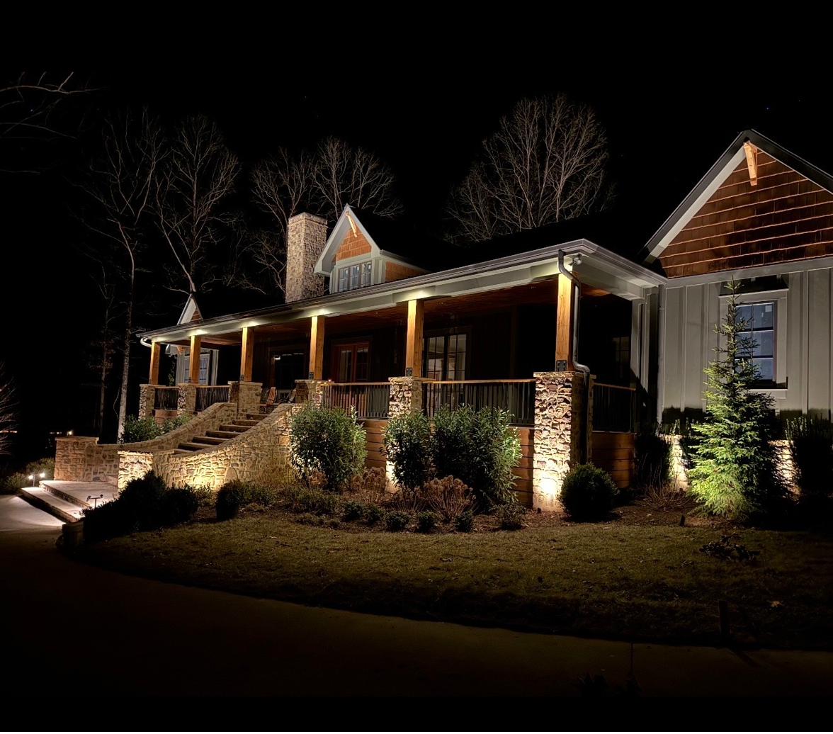 Stone farmhouse with custom porch lighting and foundation plantings at night