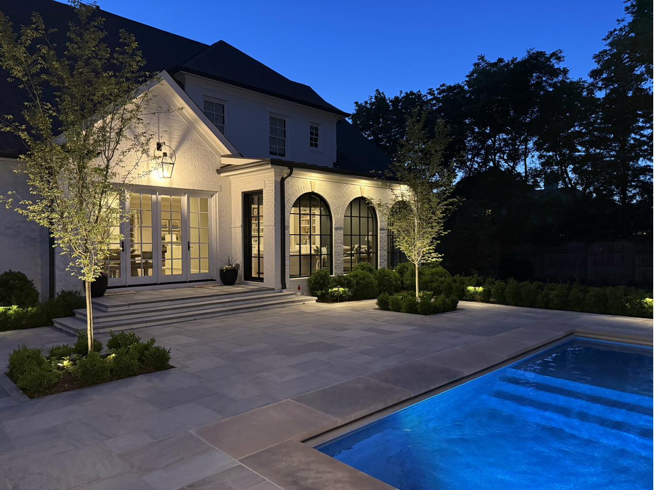 White brick estate with arched windows and pool surround plantings lit at blue hour