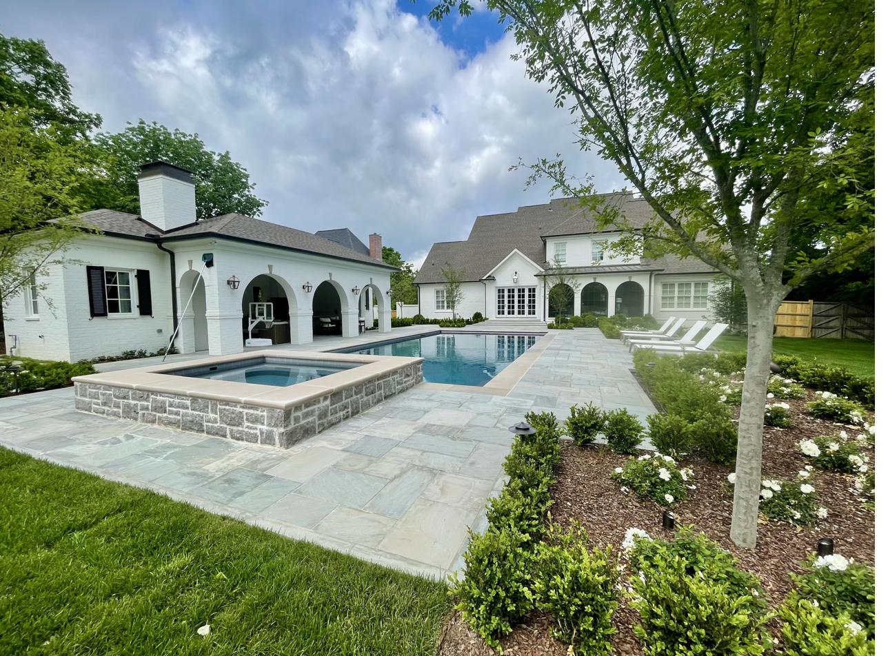 White estate with arched pool house, bluestone patio, and rose garden plantings