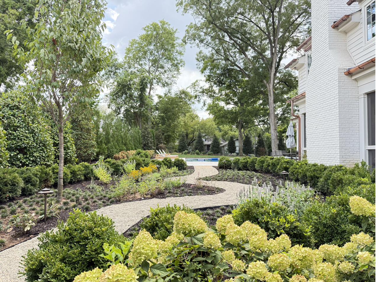 Winding gravel path through hydrangea and boxwood garden beds in daytime