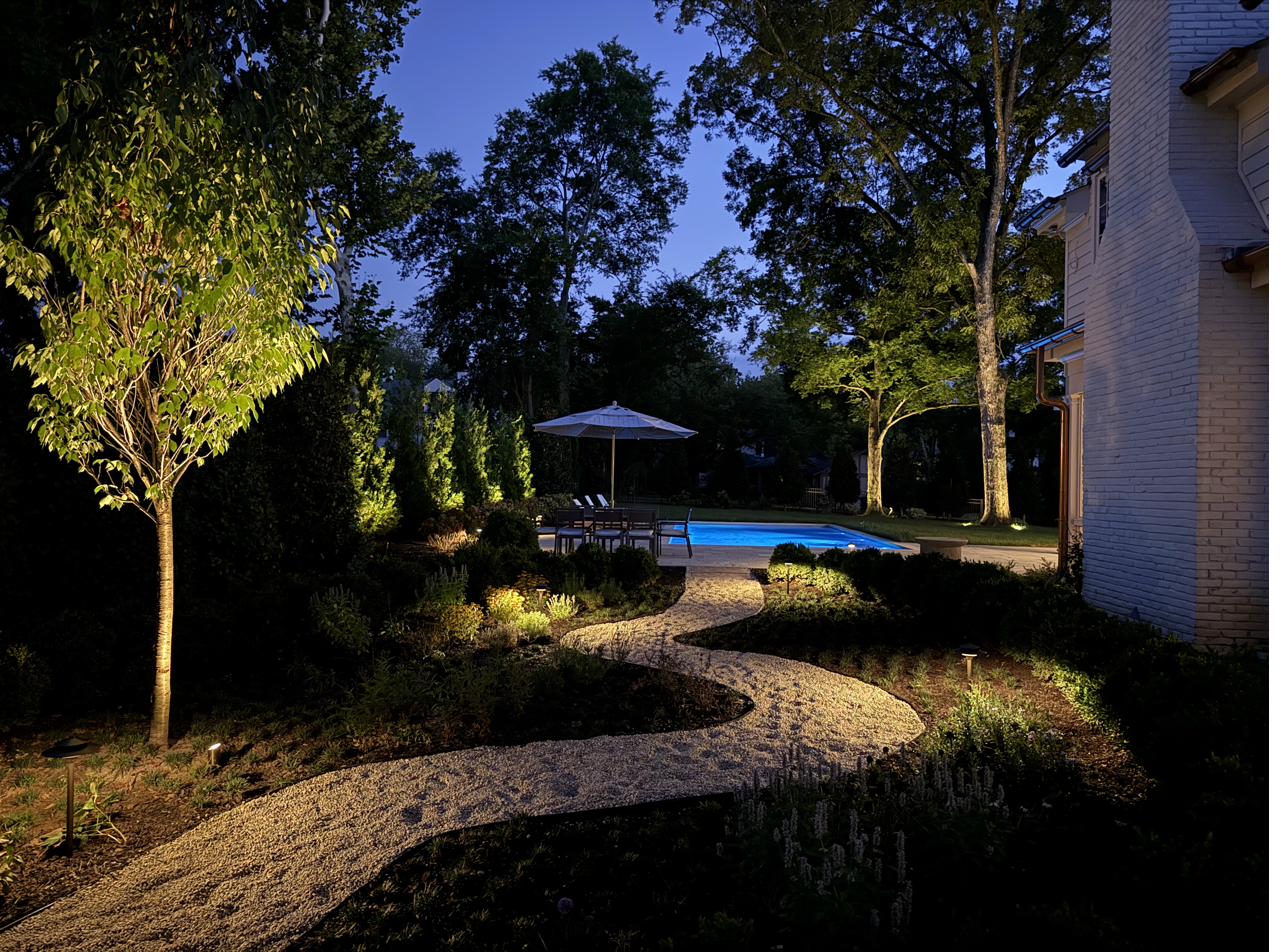 Winding gravel path with path lights leading to illuminated pool and garden at night
